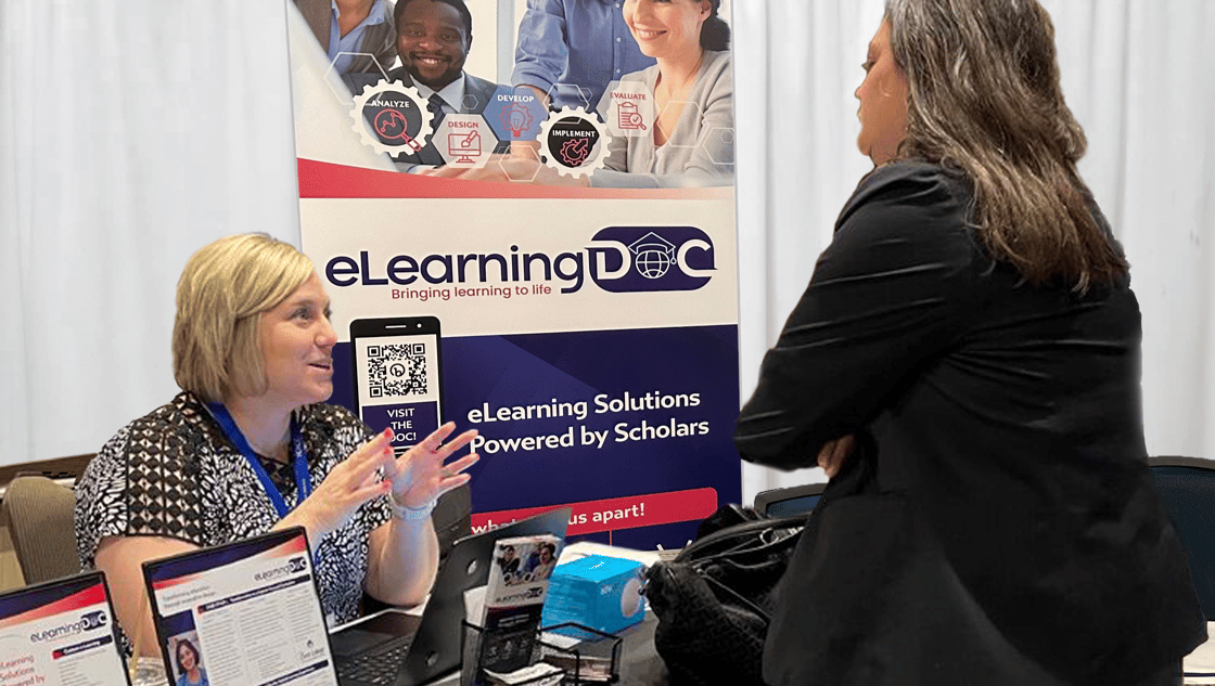 Dr. Robbins at the eLearningdoc conference booth speaking with an attendee.